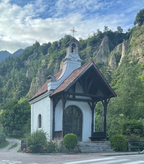 Small white chapel with bell tower nestled in mountainous forested landscape