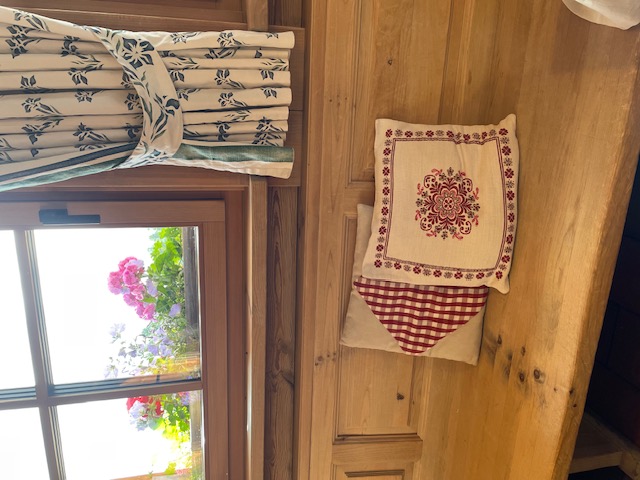 Wooden bench with decorative cushions near window with colorful flowers