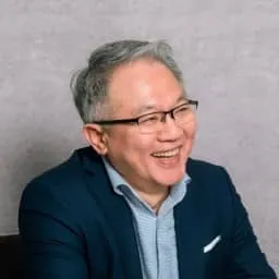 Portrait of Alex Kuo smiling and wearing glasses in a navy-blue suit jacket and a light blue shirt.