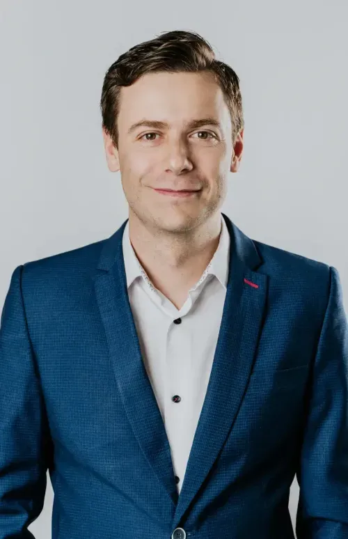 Portrait of Maciej Teska, CEO of Synergy Codes: a data visualization agency, wearing a blue suit jacket and a white shirt, smiling and looking directly at the camera