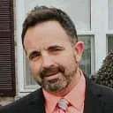 Profile picture of Jason Stewart with short dark hair and a beard, wearing a dark suit and a peach-colored shirt.