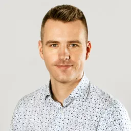 Portrait of Lukasz Jazwa, CTO at Synergy Codes with short brown hair, wearing a light-colored patterned shirt, smiling at the camera.