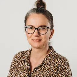 Portrait of Anna, a female UX/UI designer wearing glasses and a patterned shirt.