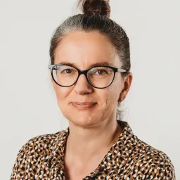 Portrait of Anna, a female UX/UI designer wearing glasses and a patterned shirt.