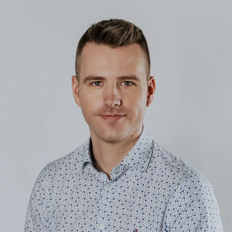 Portrait of Lukasz Jazwa, CTO at Synergy Codes with short brown hair, wearing a light-colored patterned shirt, smiling at the camera.