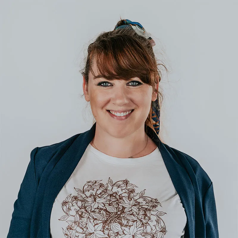 A portrait of Paulina Kondratowicz, a cowriter of GoJS, with brown hair tied up in a ponytail with a colorful scarf. She wears a navy blue blazer over a white shirt with a detailed floral illustration. 