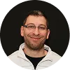 Smiling man with short dark hair, glasses, and a beard wearing a light hoodie.