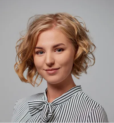 Smiling woman with short curly blonde hair wearing a striped shirt with a bow collar.