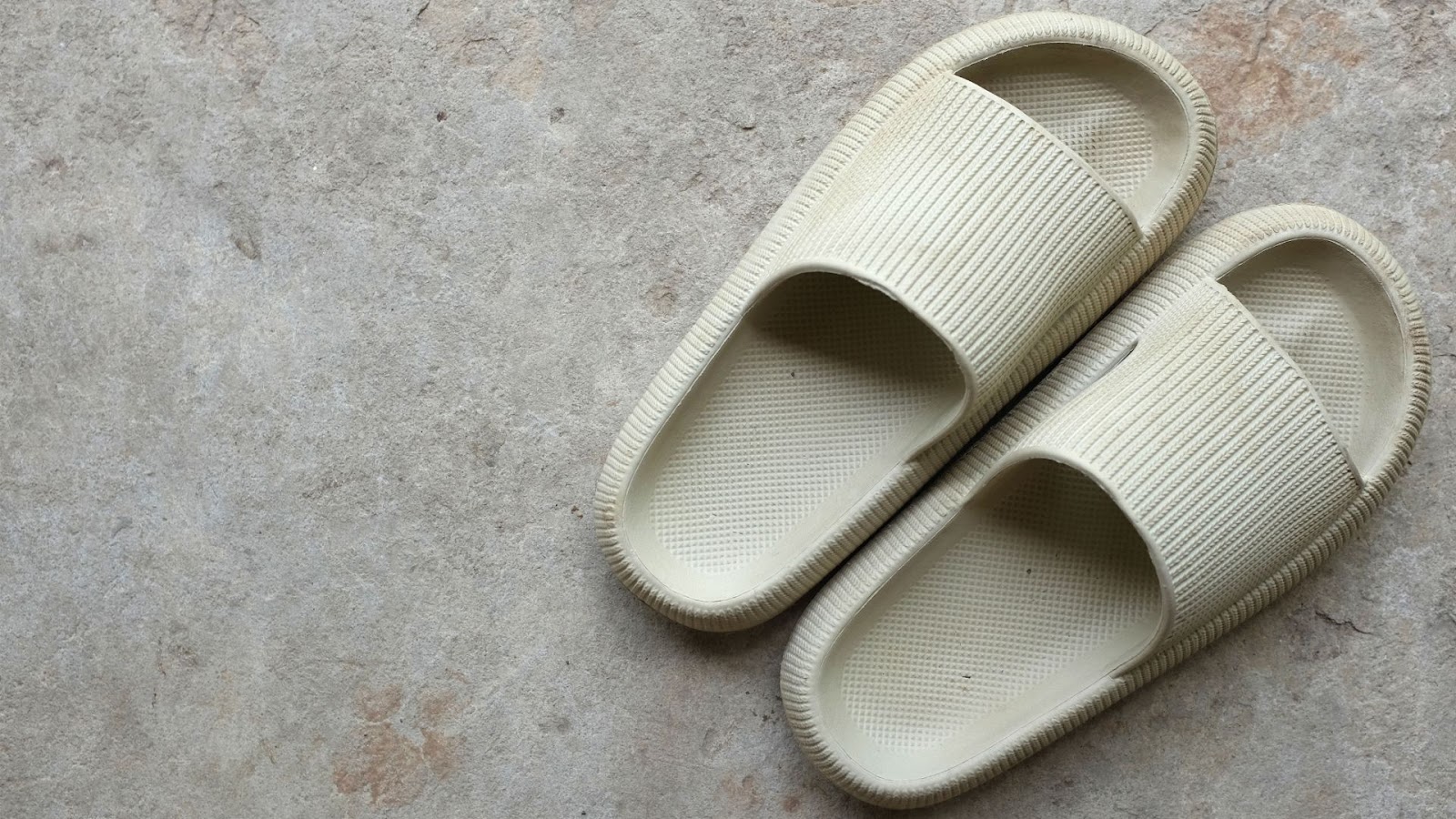 Pair of white cream rubber slides resting on a gray background.