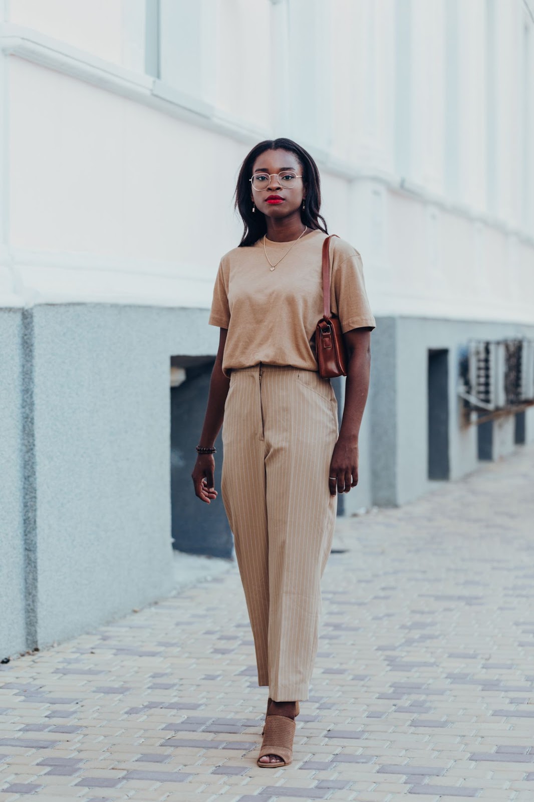 A woman wearing a monochrome brown outfit with pants and a t-shirt, sandals, and a bag.