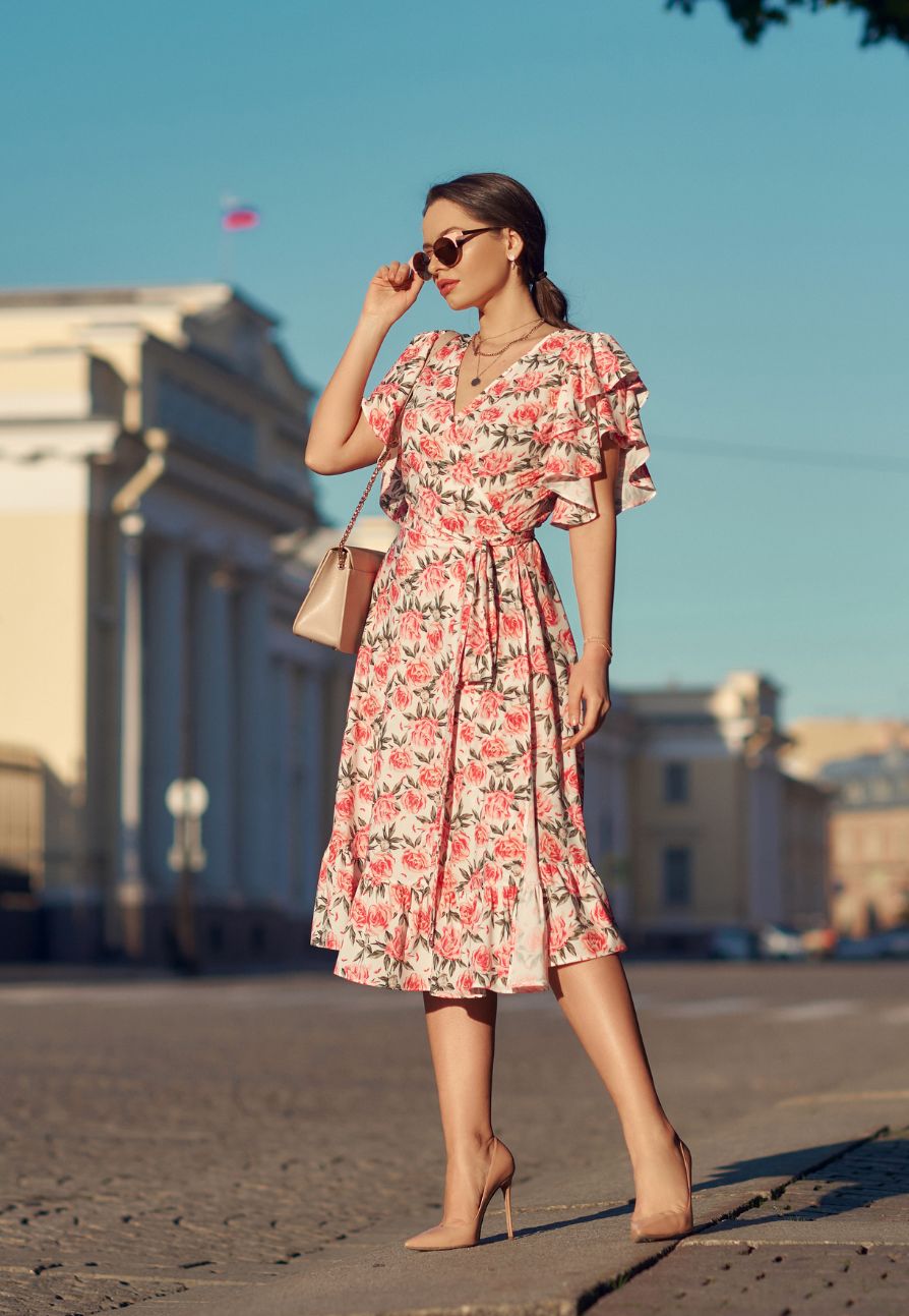 A woman wearing a floral tailored midi dress with high heels, a bag, and sunglasses.