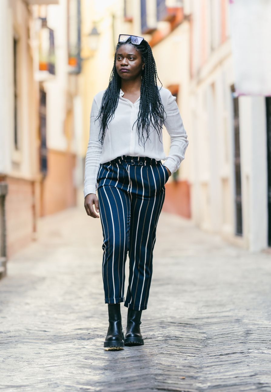 A woman wearing blue vertical striped pants with a white shirt, boots, and sunglasses.