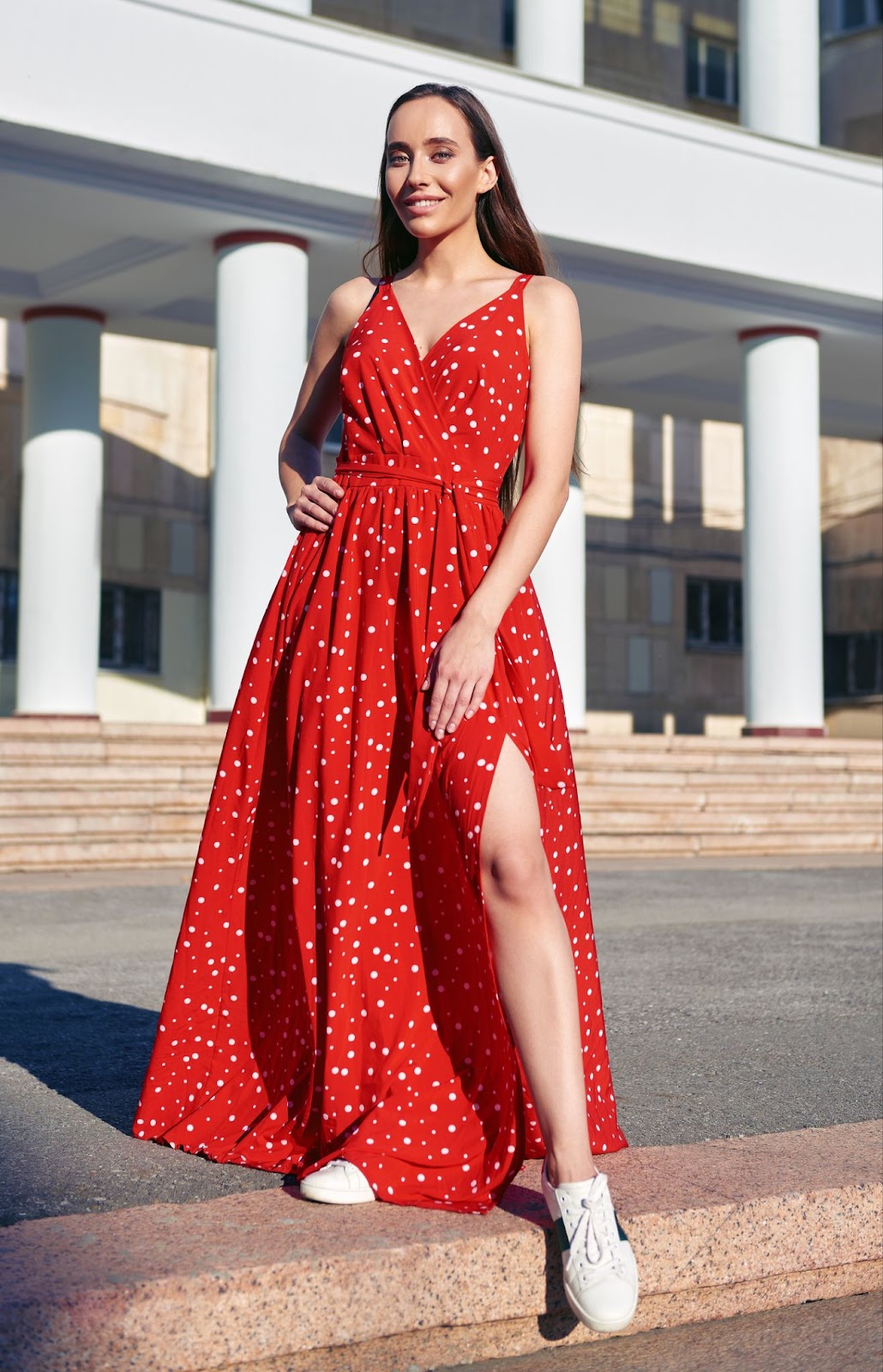A woman wearing a red maxi dress with a hemline and white sneakers.