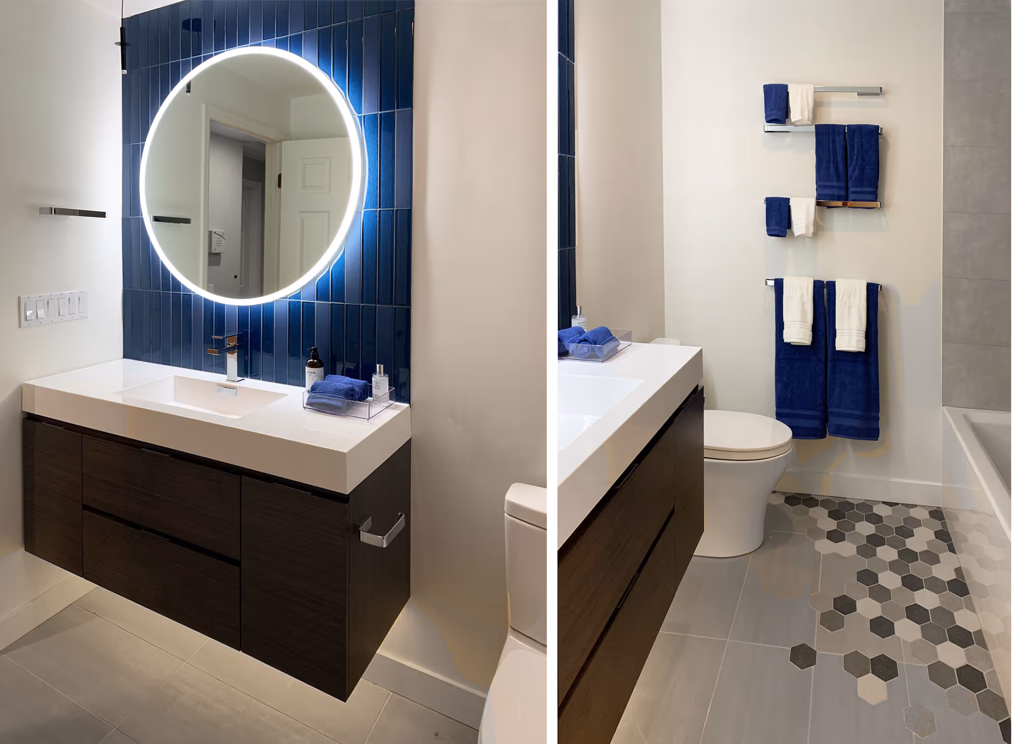 A modern bathroom with sleek design elements. The left side of the image features a floating vanity with a white countertop and dark wood cabinetry, complemented by a round, illuminated mirror mounted on a wall of vertical blue tiles. The right side of the image shows a view of the bathroom's toilet and a towel rack holding blue and white towels. The floor features hexagonal tiles in shades of gray and white, leading to a bathtub with a gray tile surround. The overall design is contemporary and stylish, with a focus on clean lines and contrasting colors.