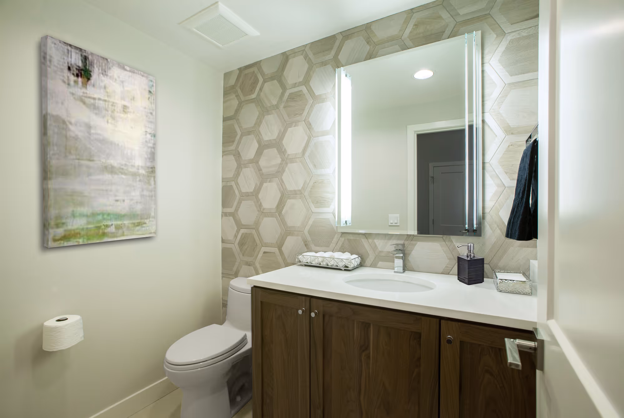 Modern bathroom with hexagonal patterned wall, wooden vanity, mirror, toilet, and abstract painting.
