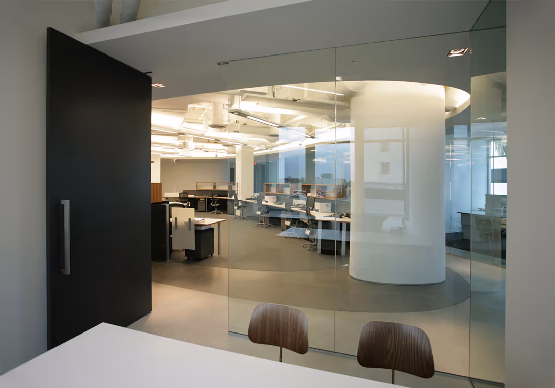 Modern office with glass walls, open workspace, and two wooden chairs at white table.