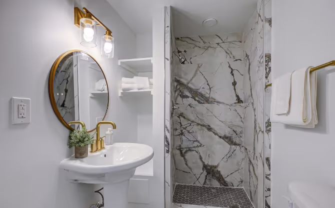 Renovated bathroom featuring grey mosaic tiles on the shower floor, glass shower enclosure, modern fixtures, and a sleek, contemporary design