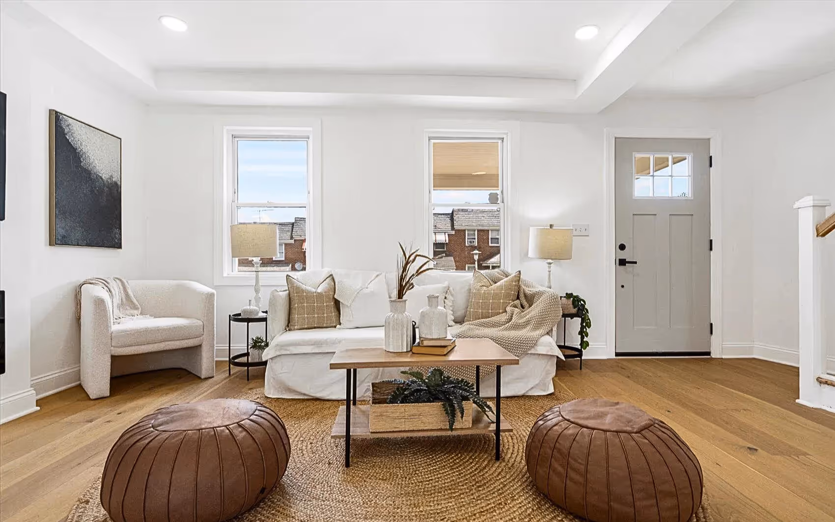 Bright living room with white walls and plank flooring throughout, featuring a newly installed front door painted grey. Two new windows provide natural light and enhance the modern, refreshed space.