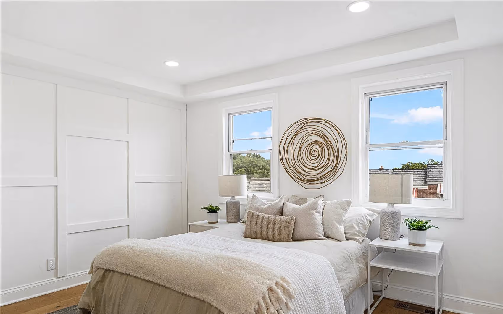 Bedroom with white walls, two new windows, and a partial view of a white accent wall featuring a square brick-patterned plank design. Room includes plank flooring and a tray ceiling.