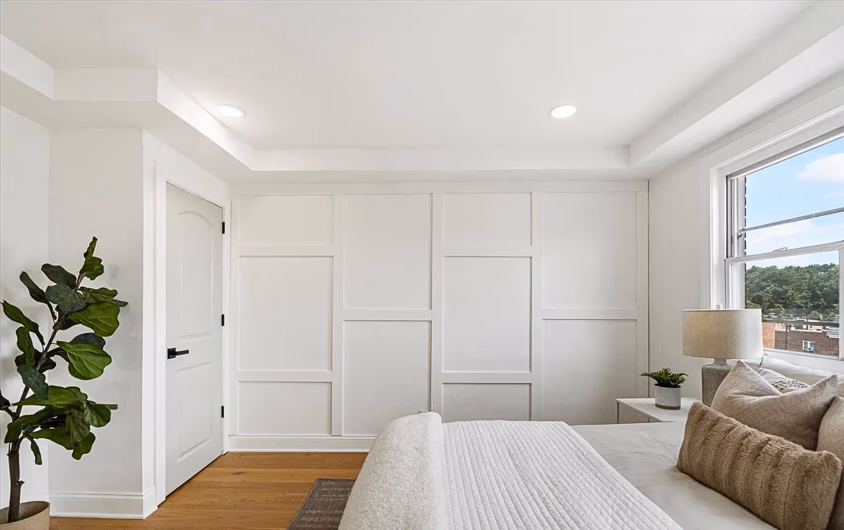 Close-up of a white accent wall with planks arranged in a square brick pattern, complemented by plank flooring and a tray ceiling in the bedroom.