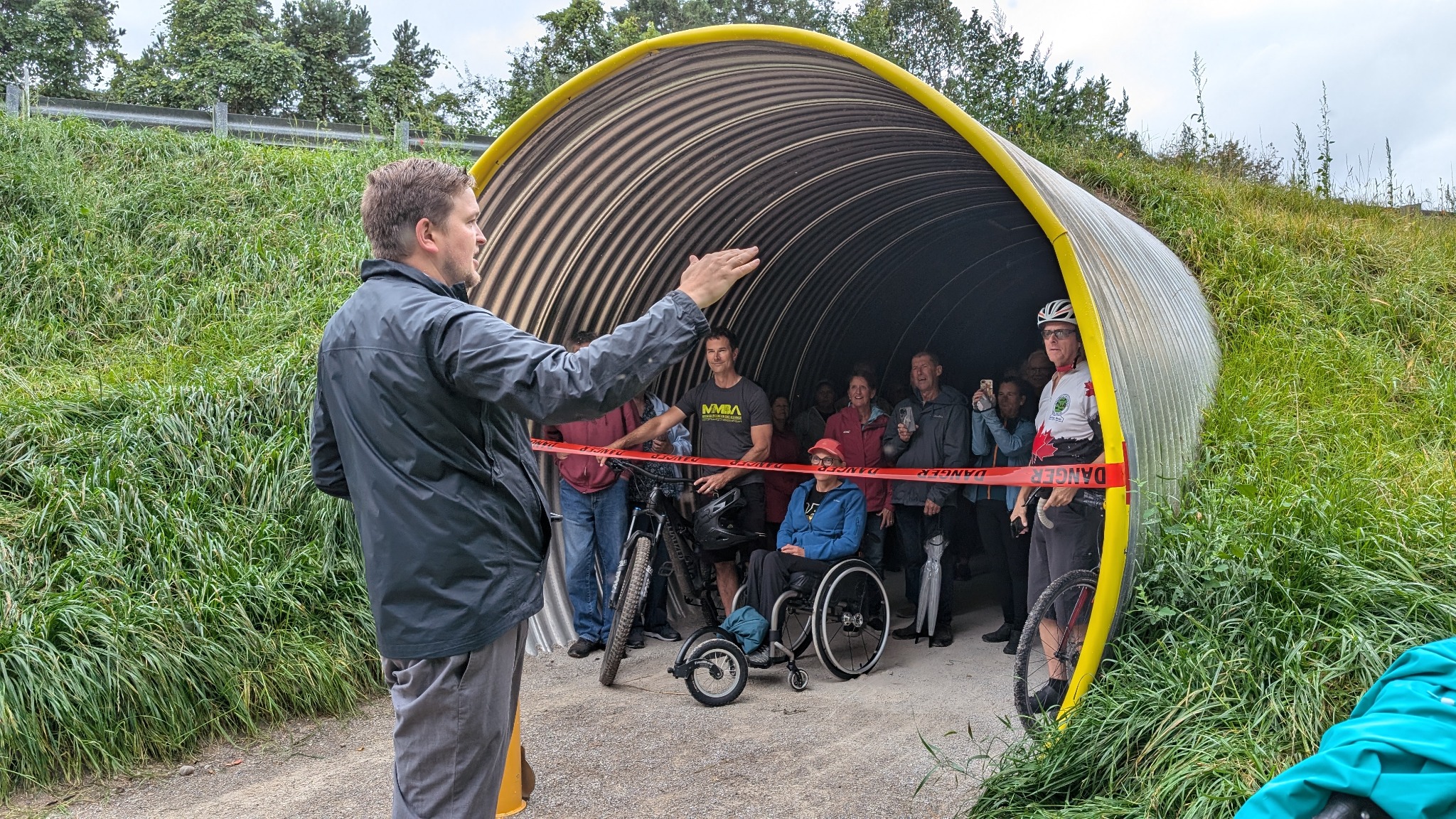 Community members gather for the Blyth Tunnel ribbon cutting, including trail users with bicycles and a wheelchair.