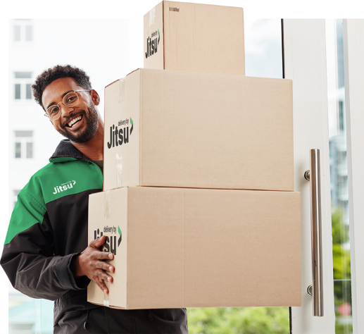 Alt text: A smiling delivery driver wearing a green and black Jitsu-branded jacket carries a stack of cardboard boxes to a doorstep. Overlaid on the image is a delivery tracking card showing "Status: Out for Delivery" with a completed progress bar, along with fields for tracking code, scheduled delivery date, and delivery address.