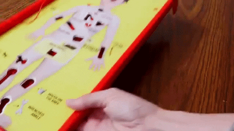 Close-up of a hand playing the classic board game Operation, reaching to remove a piece from the patient's body on the yellow game board.