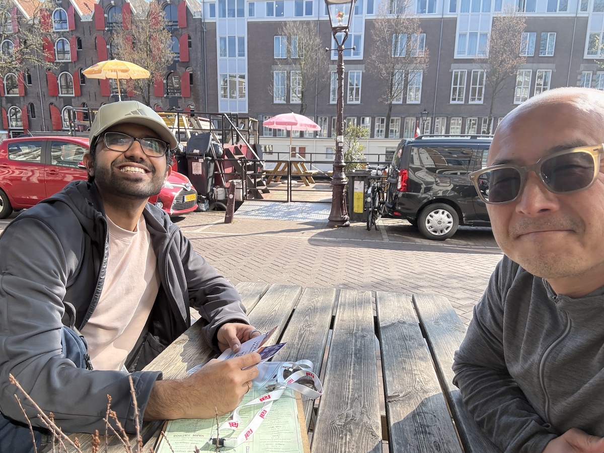 Grepr team members John and Utkarsh at an outdoor café in Amsterdam during KubeCon EU 2026.