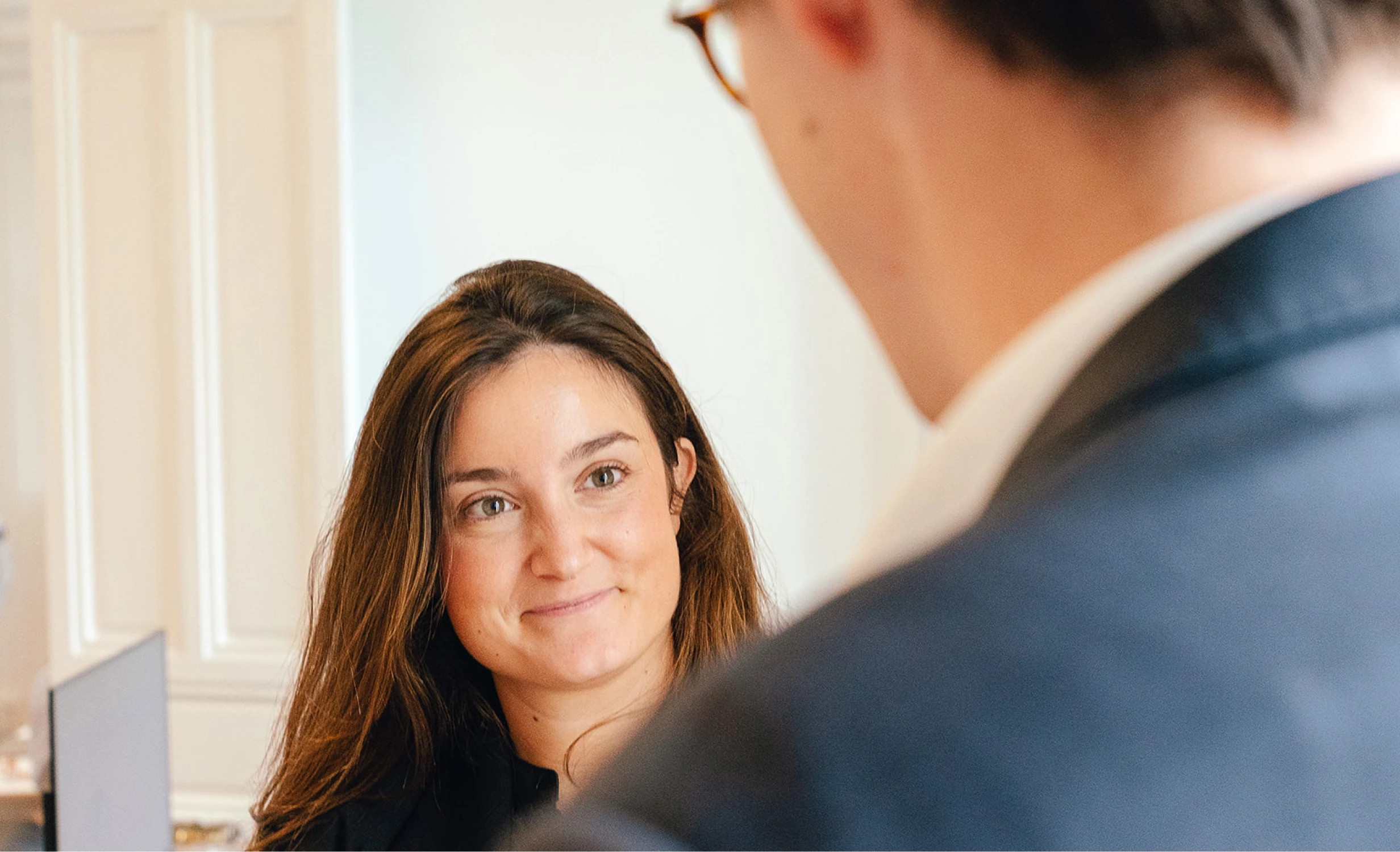 Mujer joven sonriendo mientras conversa con un colega en la oficina Transcendent luminosa en Madrid, reflejando un ambiente profesional y cercano.