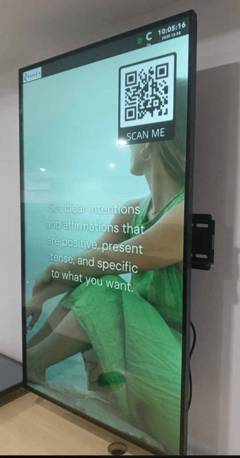 Wall-mounted portrait Android advertising screen showing content with a scan me QR code