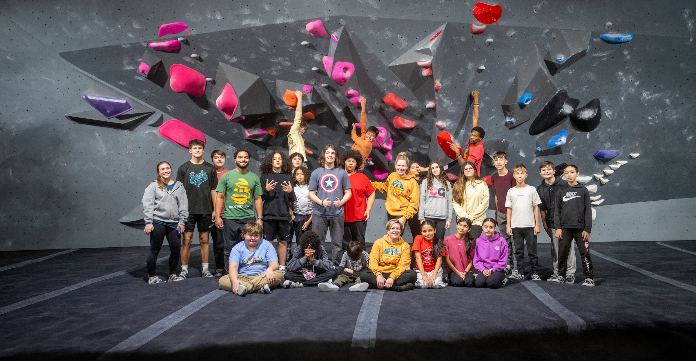 Group photo of a youth group in front of the bouldering wall at Shift Climbing gym