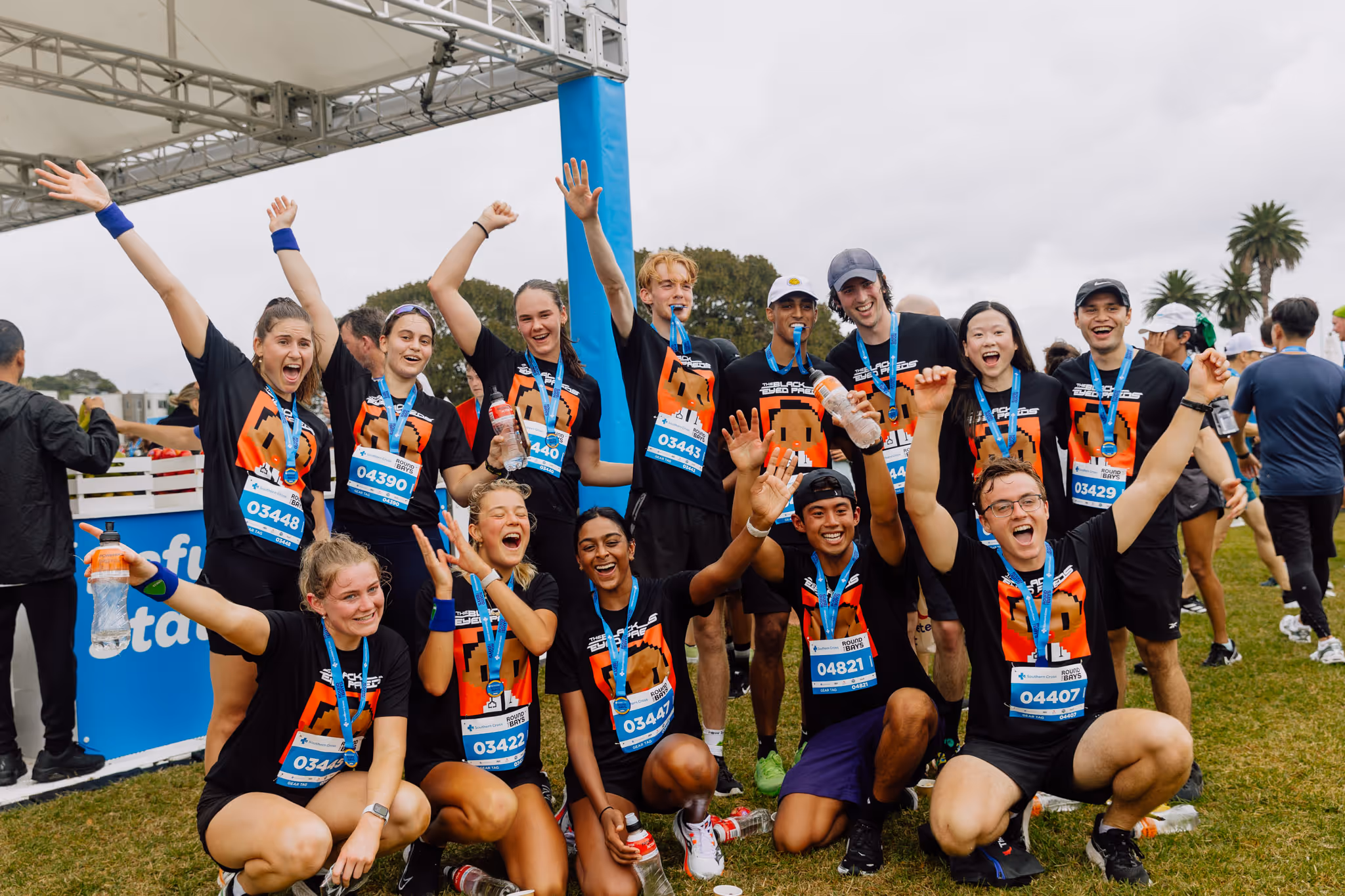 A team of people all dressed in the same tshirts celebrate completing a running race by cheering and holding their medals aloft