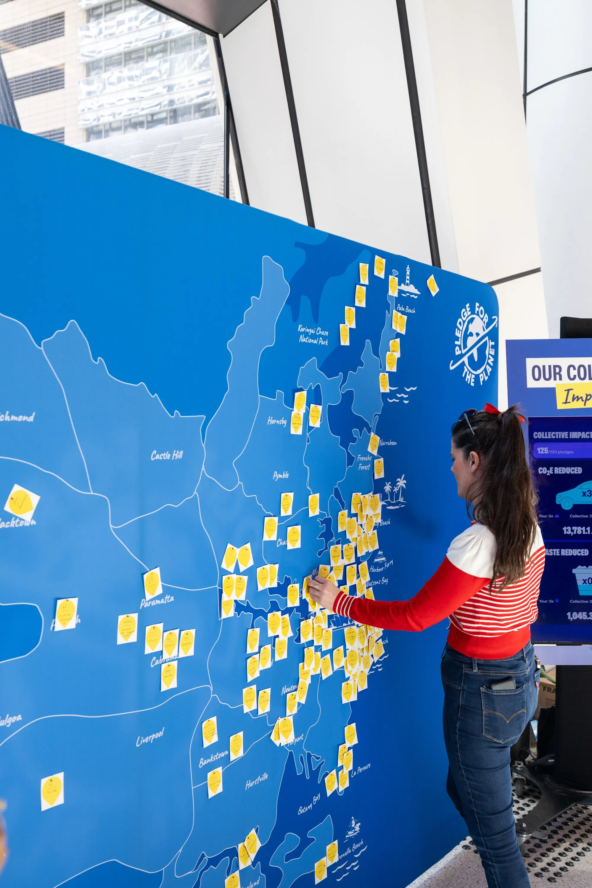 A woman adding a yellow pledge note to a large Sydney map wall