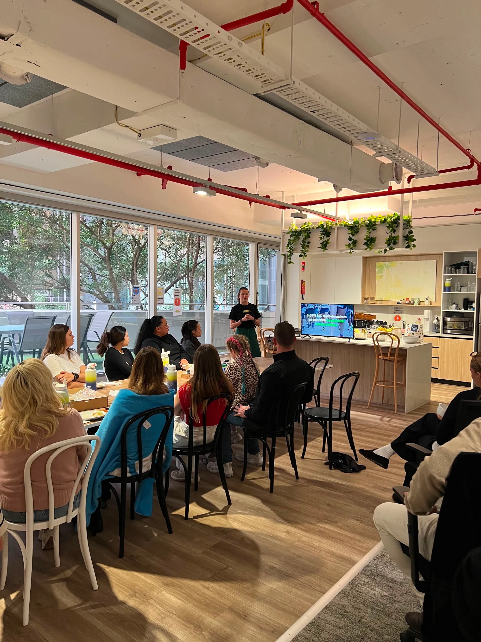 Employees seated around a table in an office kitchen listening to a Pledge workshop