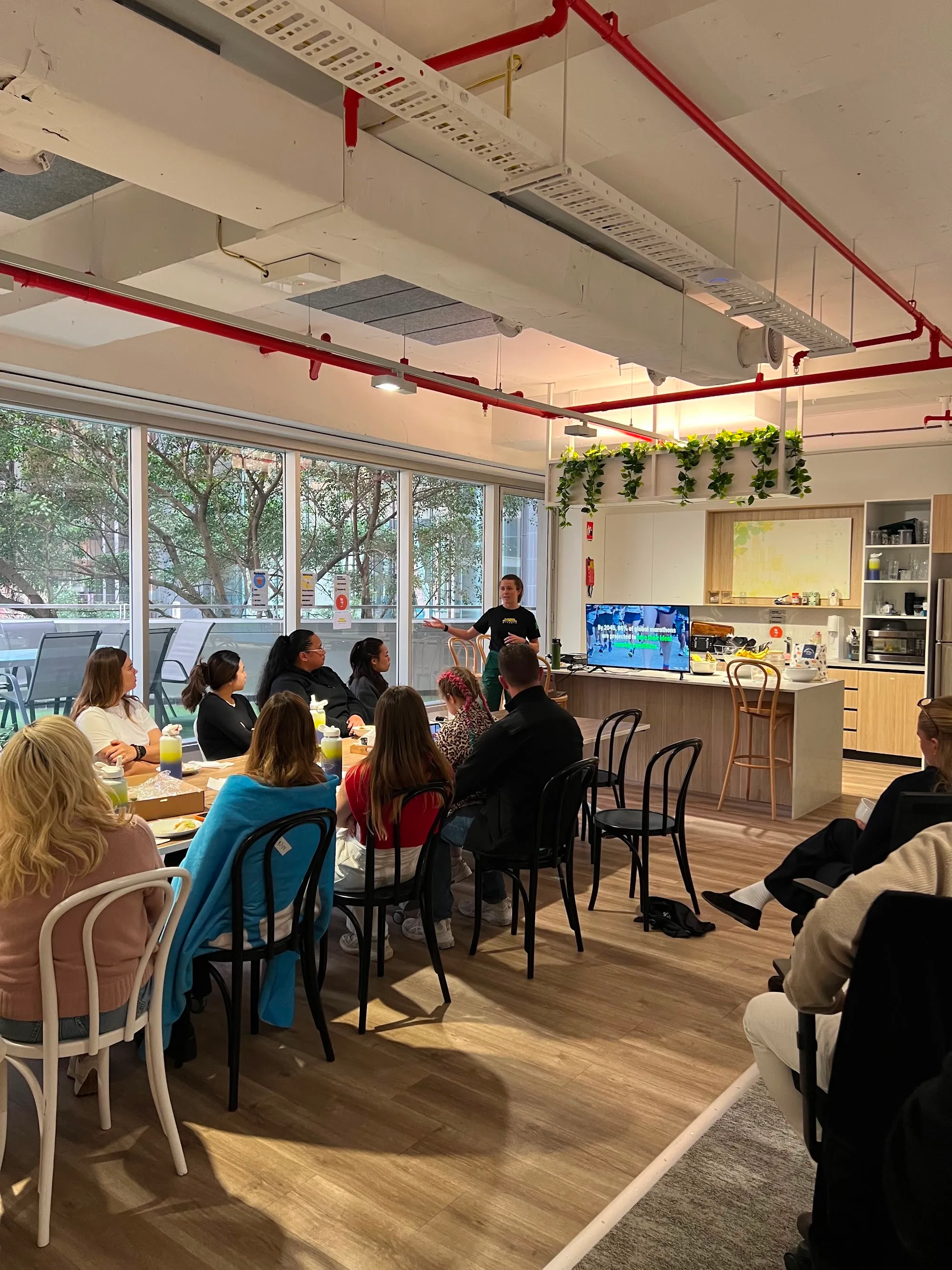 Staff seated around a table in an office breakout space watching a presentation