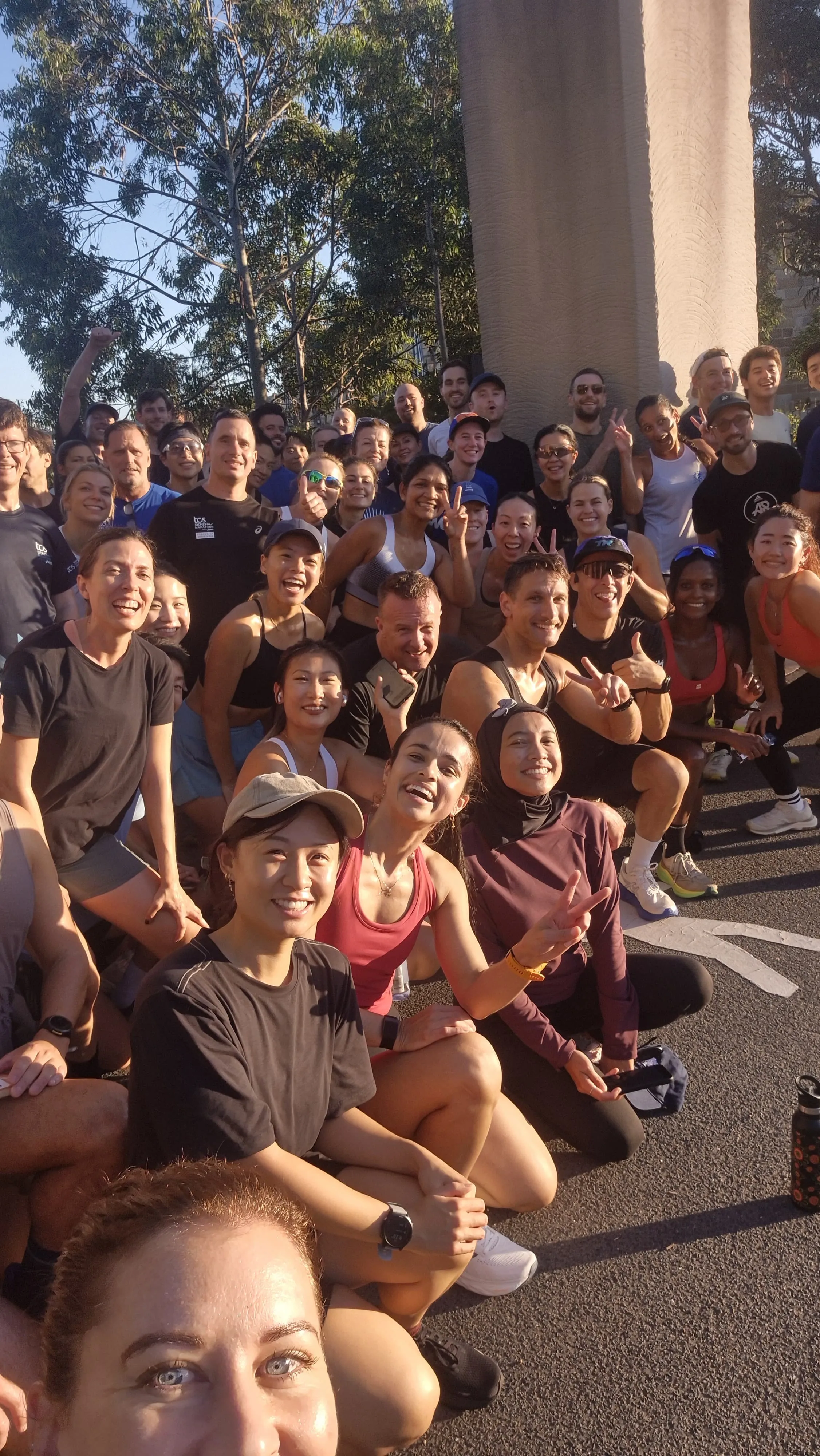 Large running group crowded together for a selfie beneath a bridge