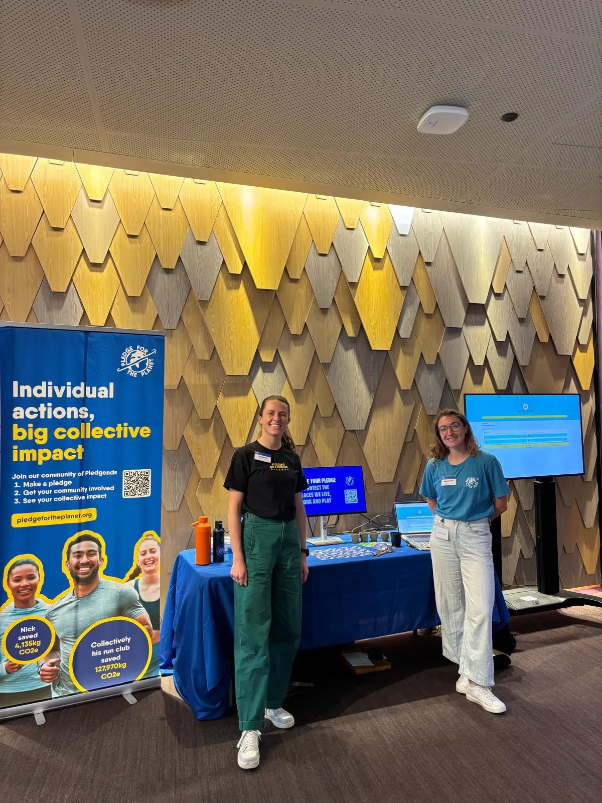 Two staff beside a stall and banner reading Individual actions, big collective impact