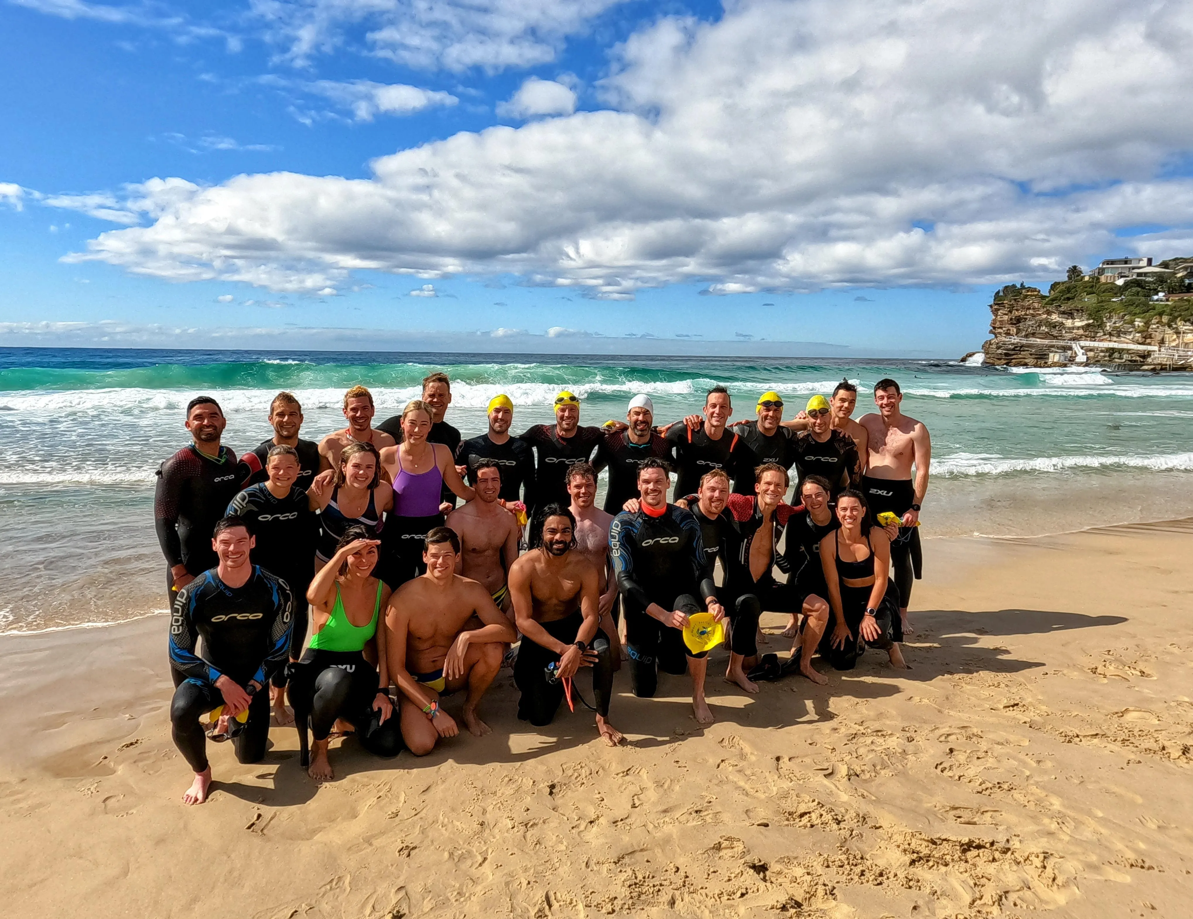 A group of ocean swimmers in wetsuits posing together on the sand after a swim