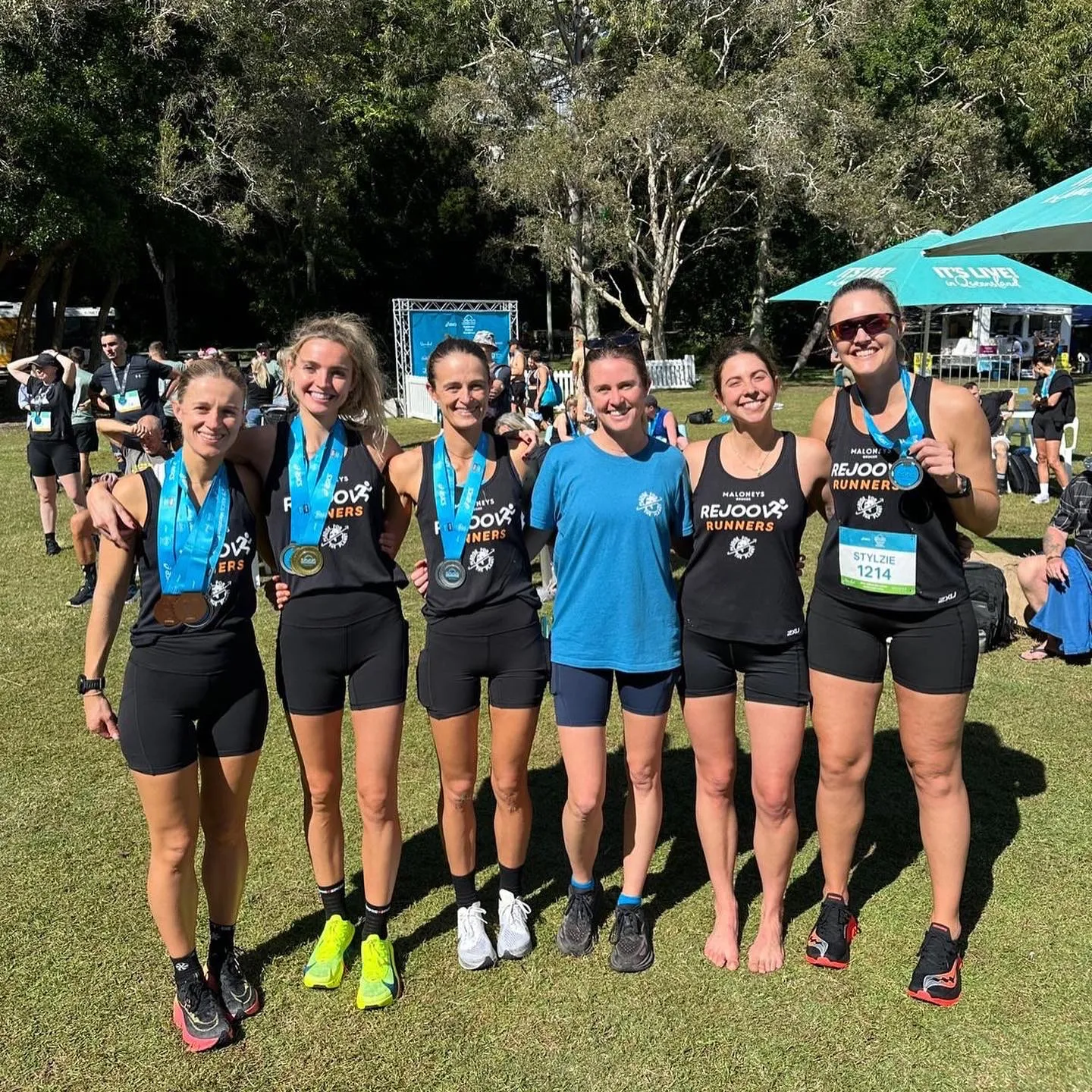 Six runners wearing finisher medals posing together on grass after a race