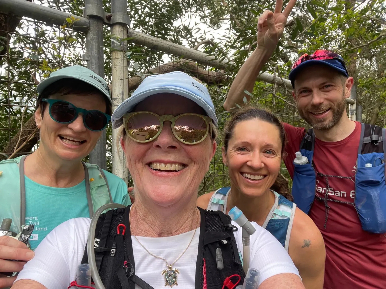 Four trail runners in caps and hydration vests smiling on a bush track