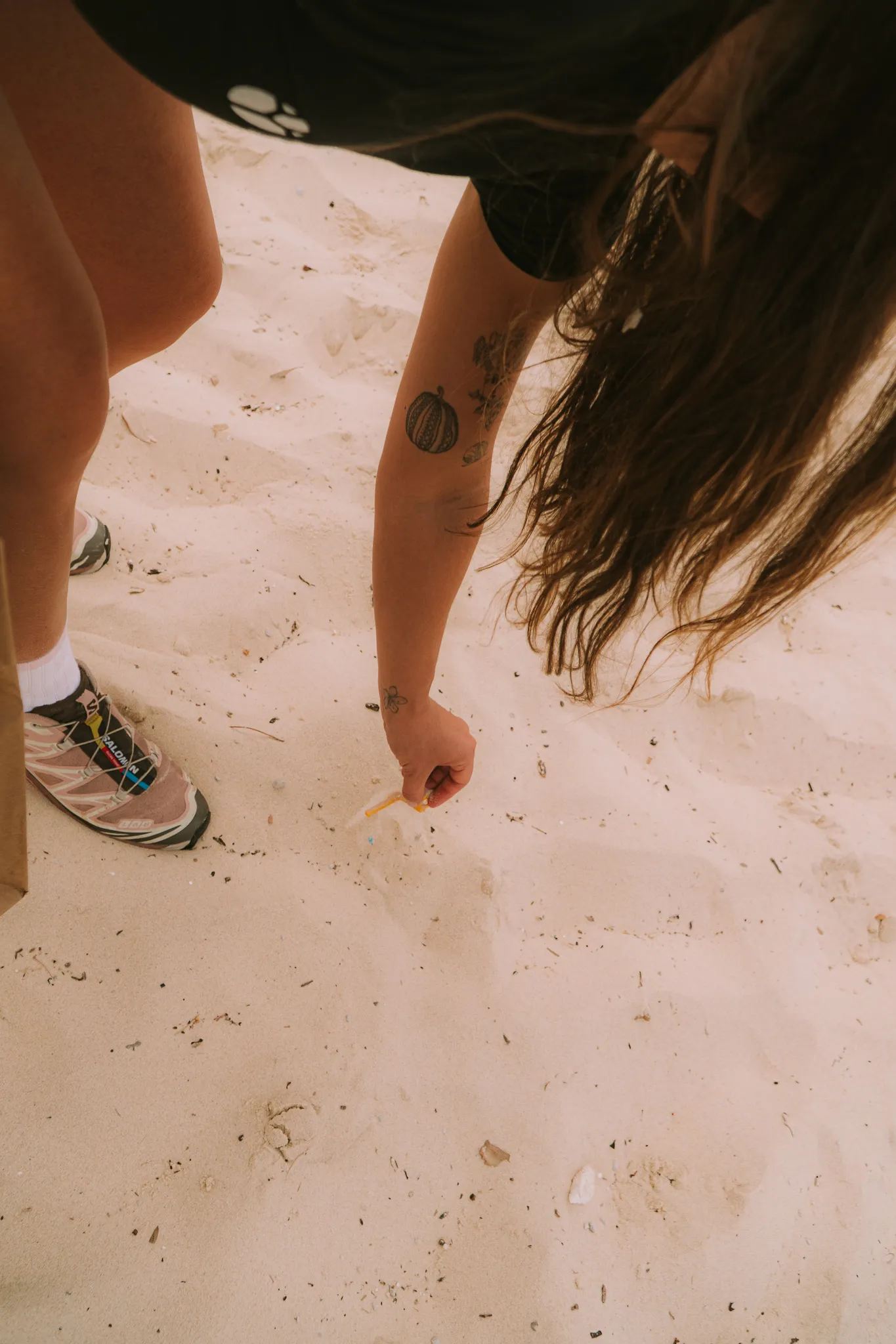 A volunteer bending down to pick up a plastic straw from the sand