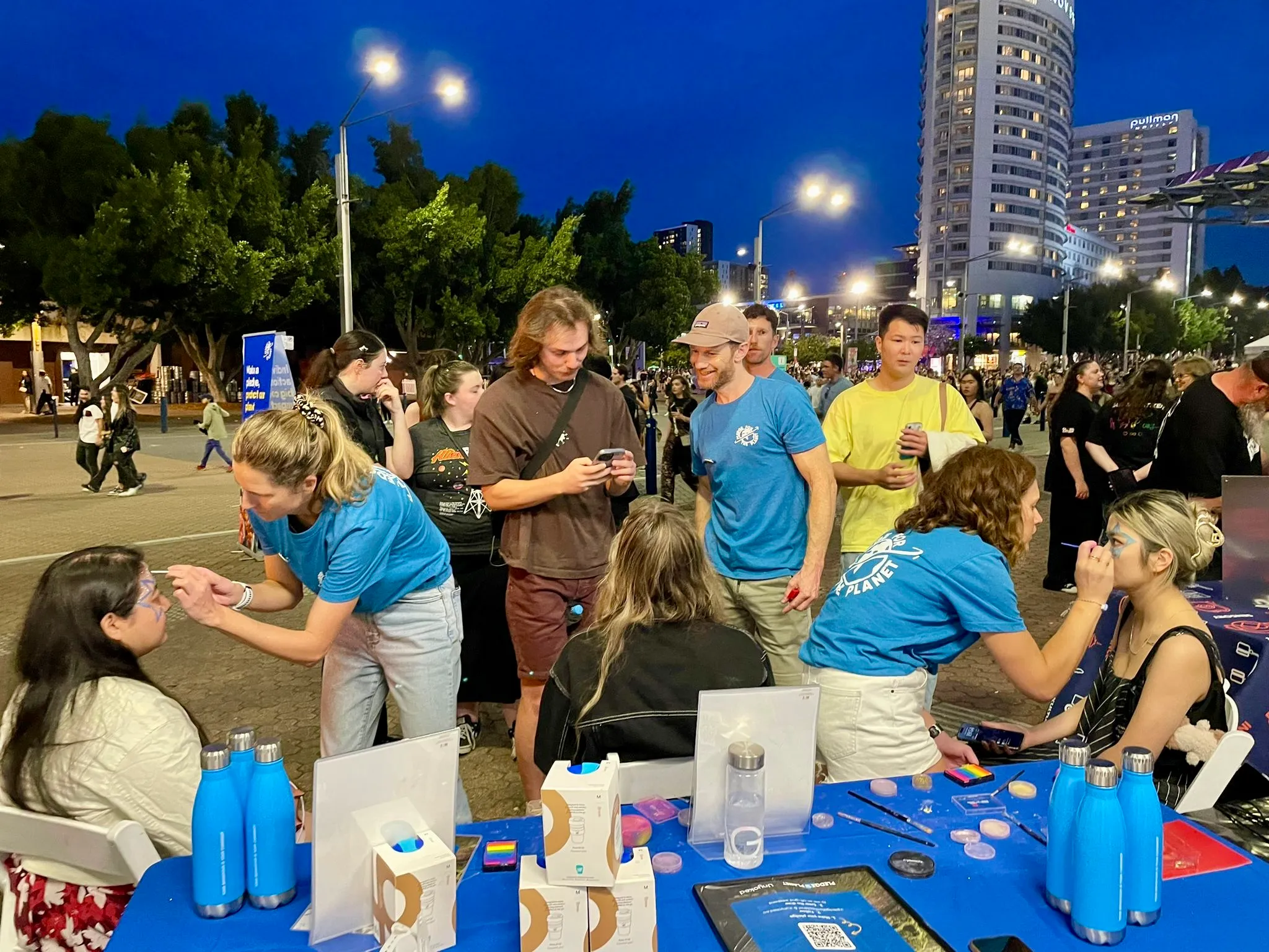 Volunteers at a lit evening event stall handing out reusable drink bottles