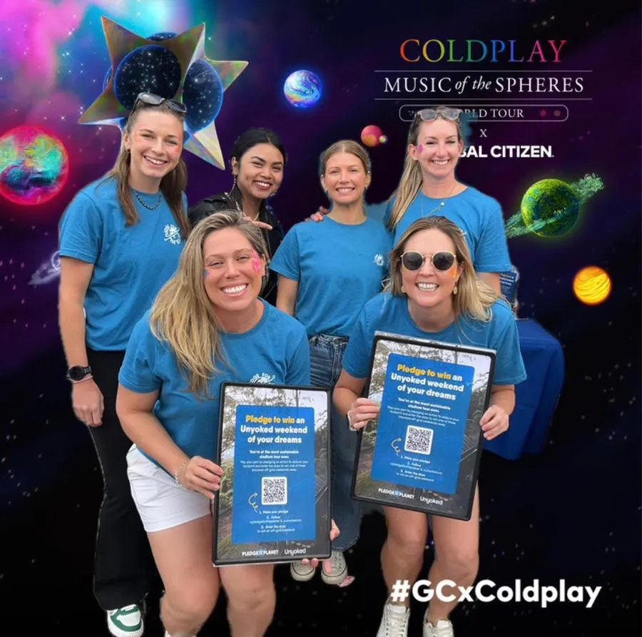 Volunteers holding pledge flyers in front of a Coldplay tour backdrop