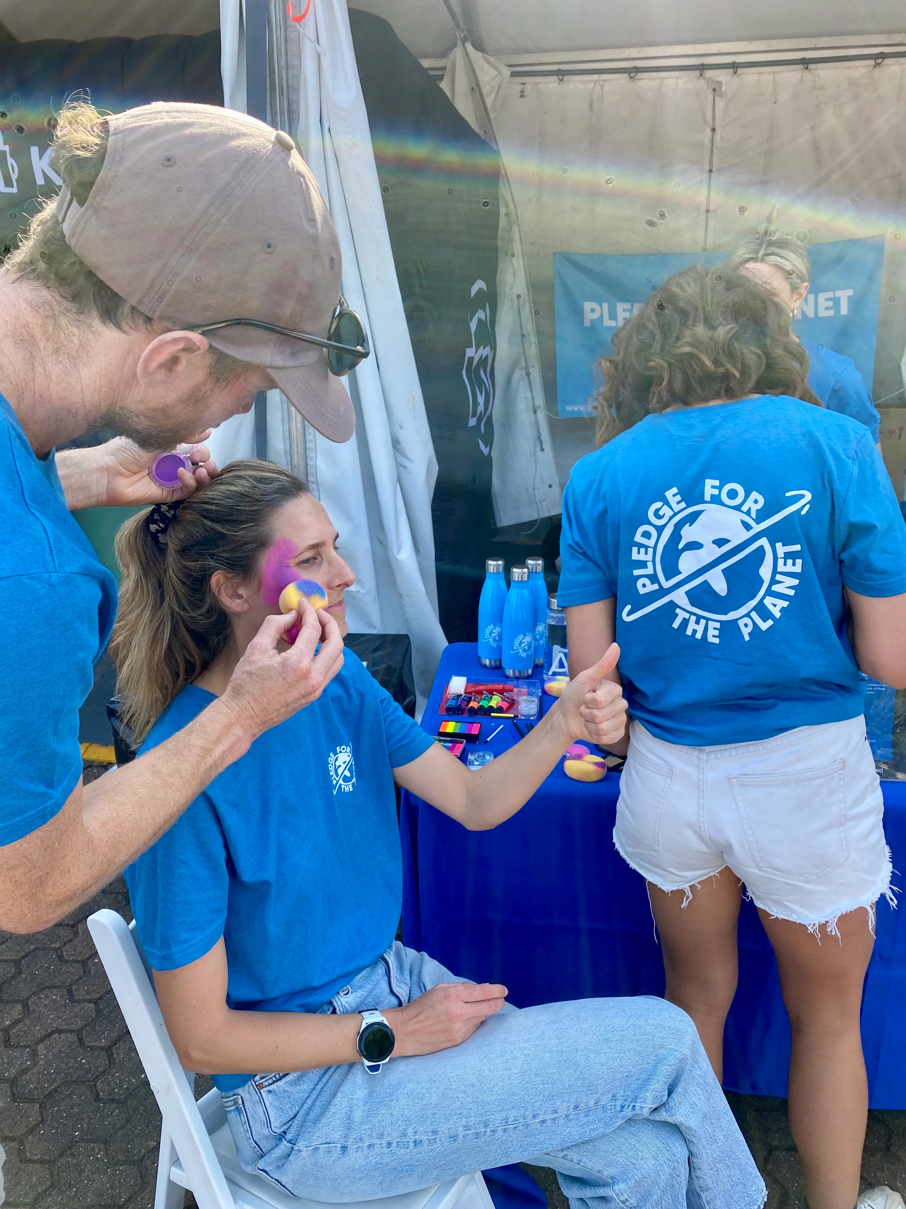 A volunteer face-painting a participant at an event stall with reusable bottles