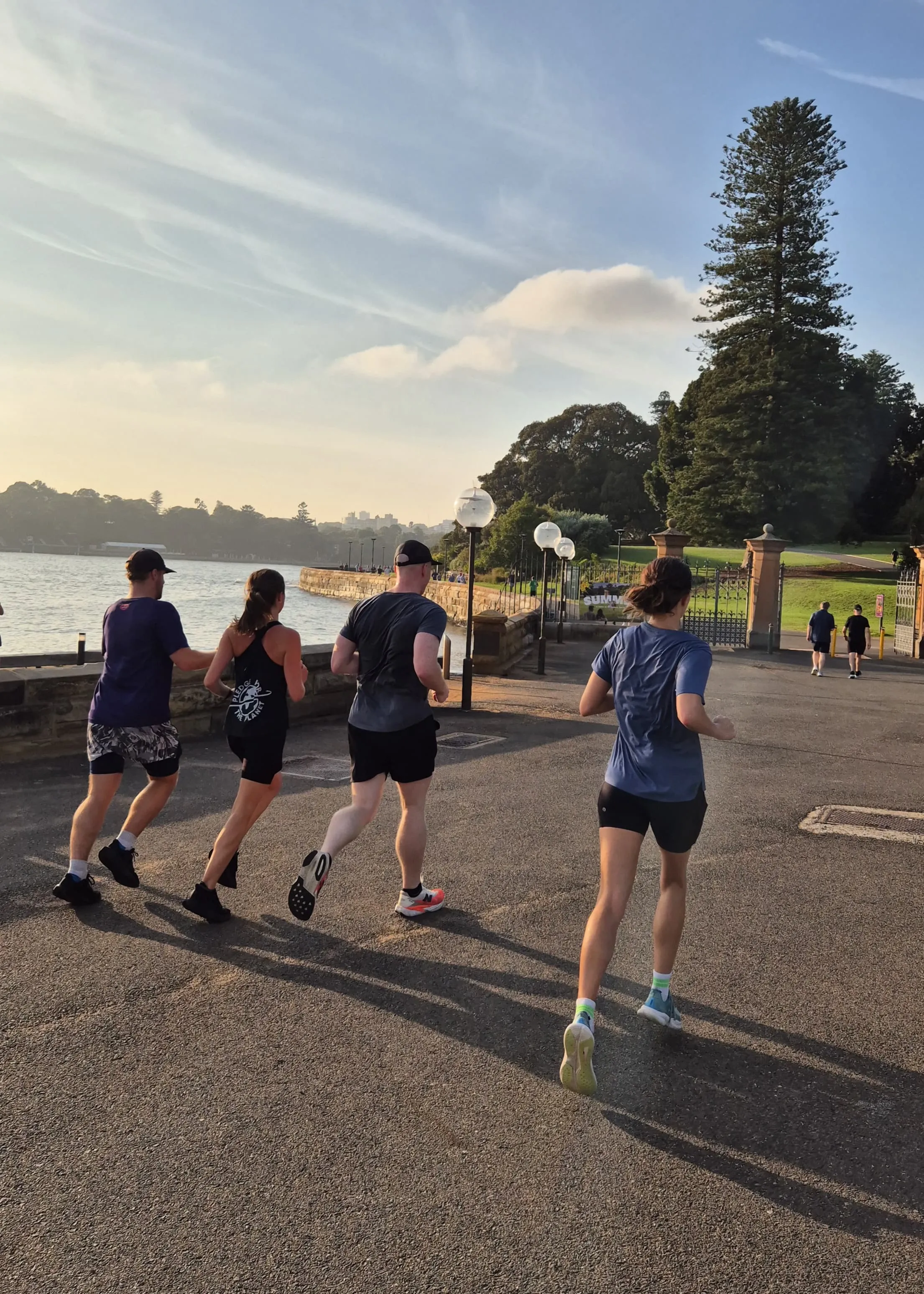 Four runners seen from behind on a harbourside path at sunrise