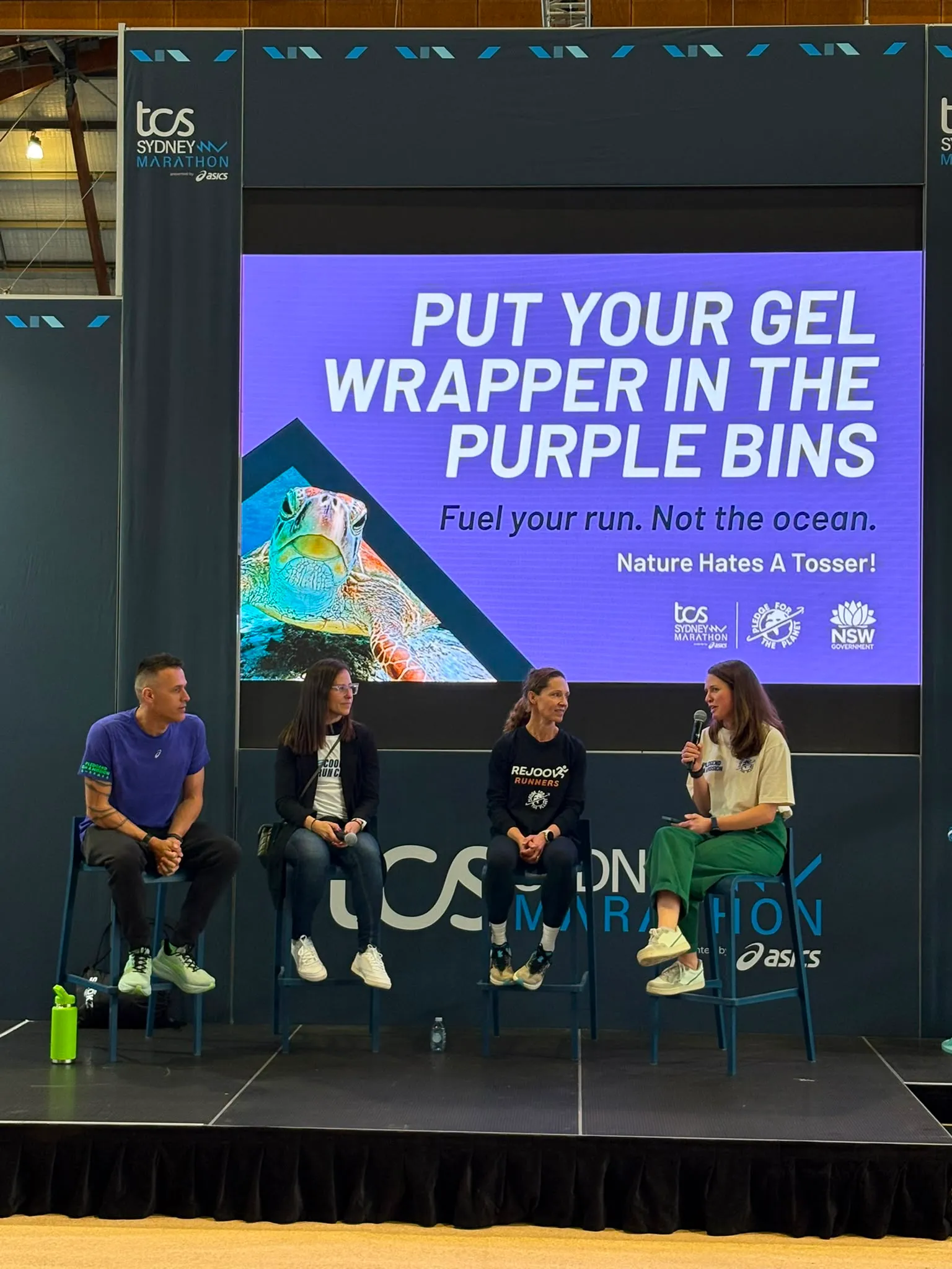 Panel discussion on stage at a marathon expo beneath a waste reduction message