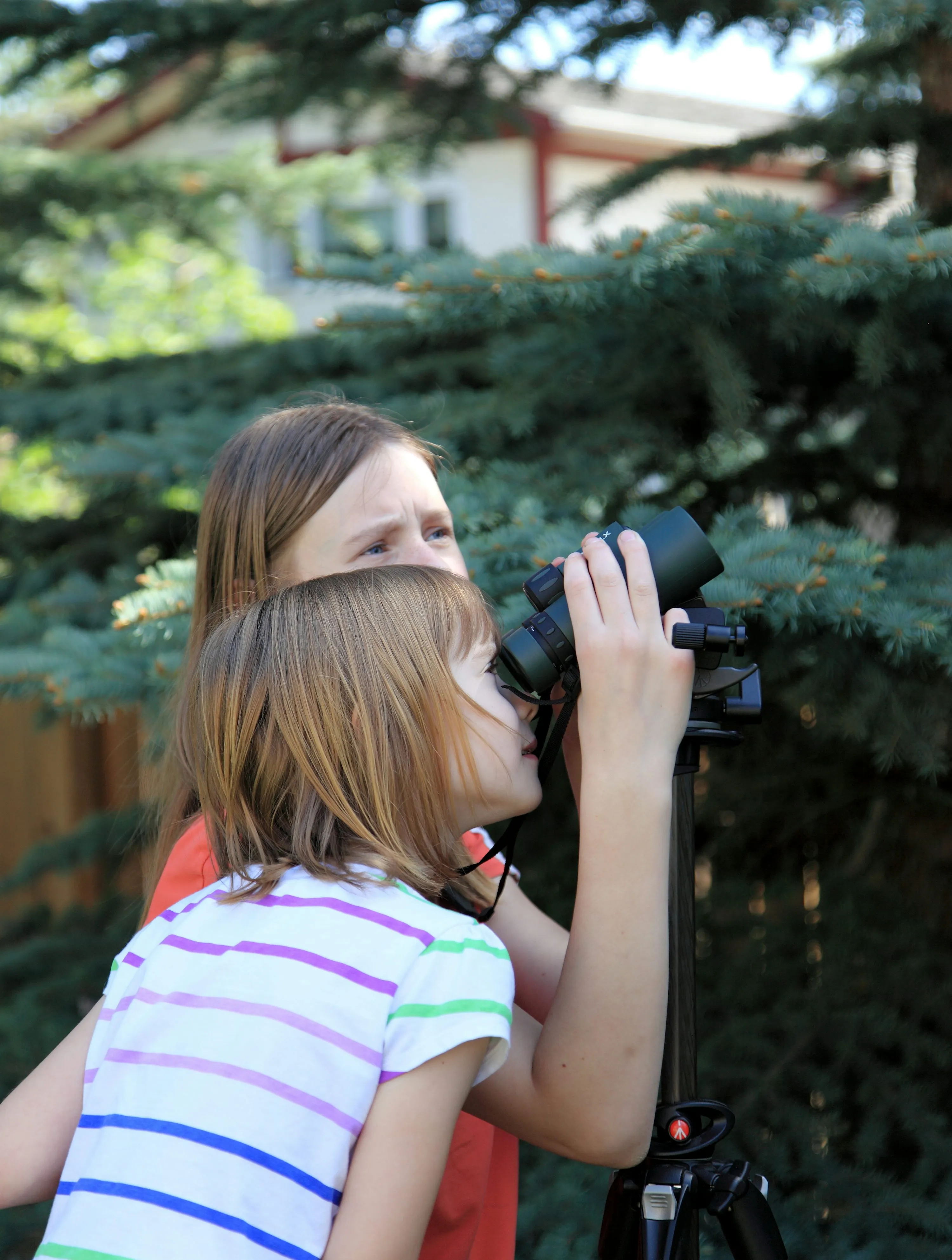 Two students sharing a pair of binoculars mounted on a tripod