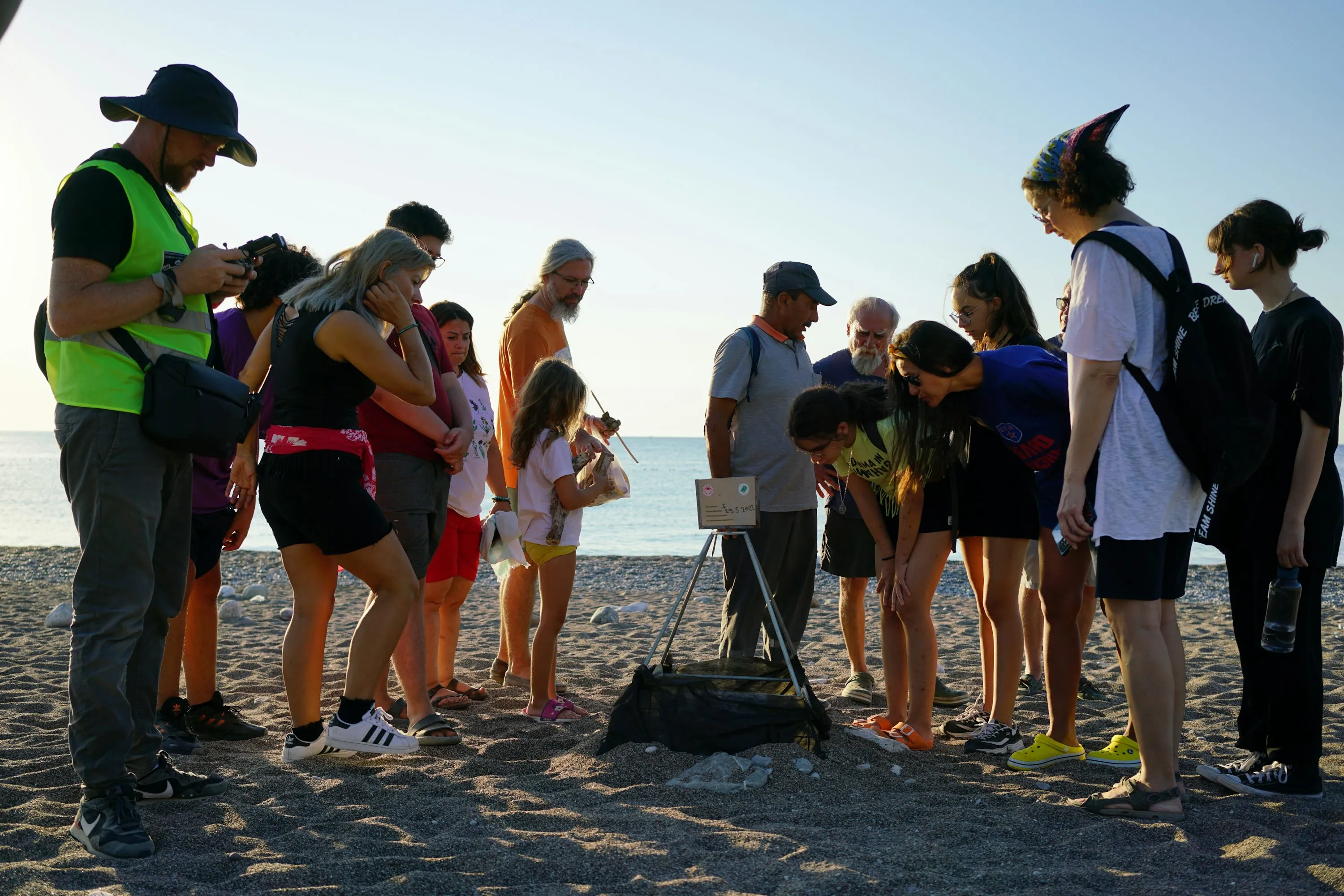 A group gathered at the water's edge on a beach at sunset