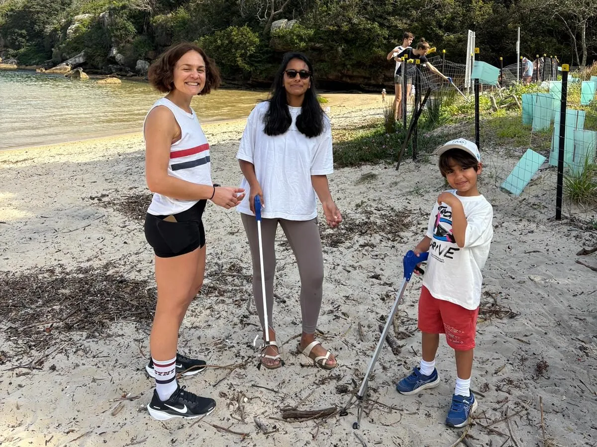 A boy with a litter picker on a harbour beach alongside two women during a beach clean
