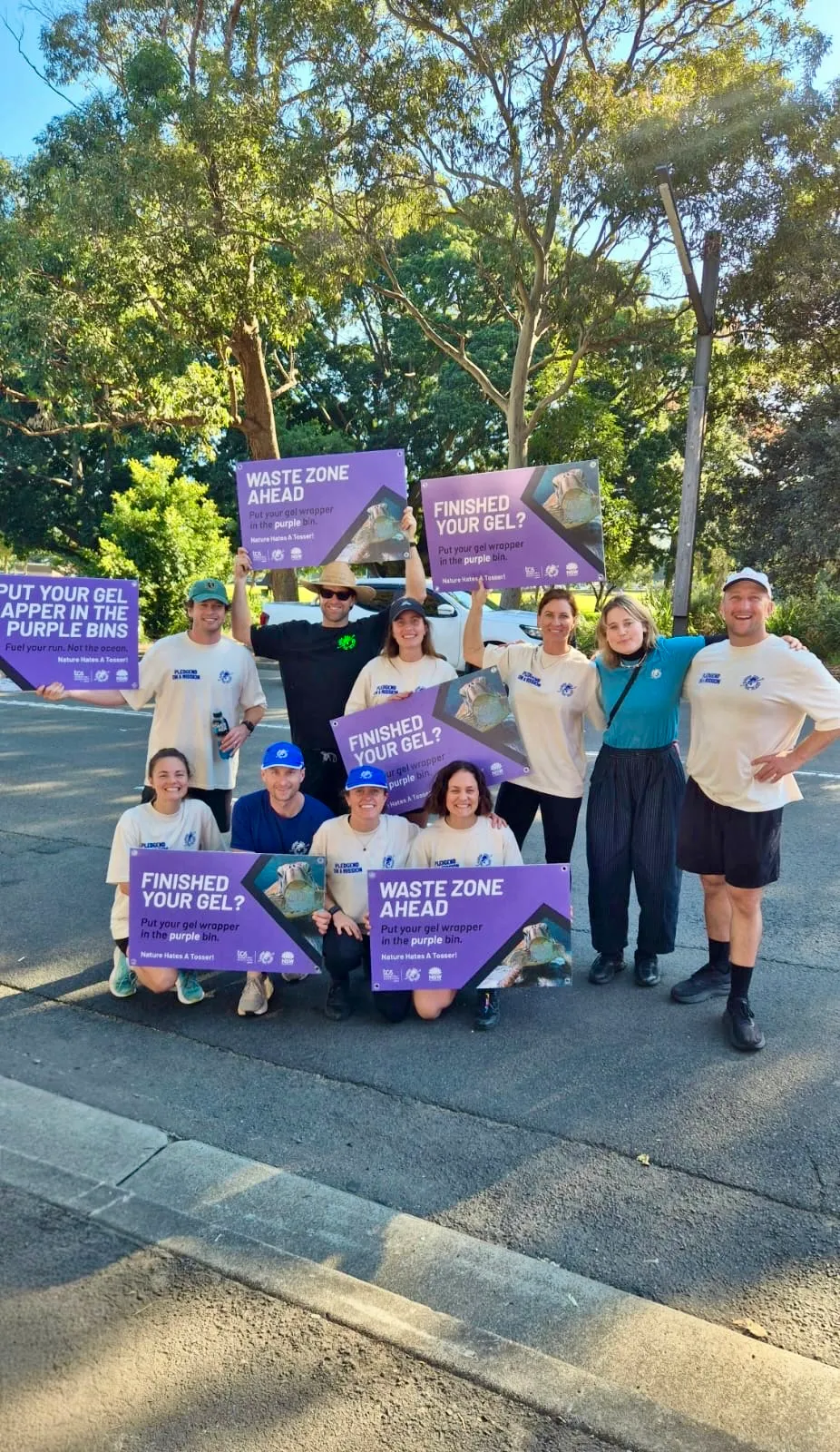 Pledge waste warriors holding purple 'Waste Zone Ahead' and 'Finished your gel?' signs at the TCS Sydney Marathon
